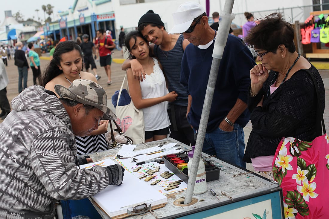Tourists watch as Santa Monica street performer Zhang Hong Cao creates artistic representations of their names at the Pier on Thursday afternoon. (Photo by Brandon Wise)