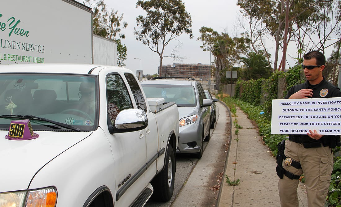 CAUGHT: SMPD Investigator Jason Olson holds a sign letting drivers know that they will be ticketed for using cell phones during a sting operation on Fourth Street on Thursday. Those busted had purple cones placed on their hoods to notify awaiting offers to issue citations. (Photo by Ashley Archibald)