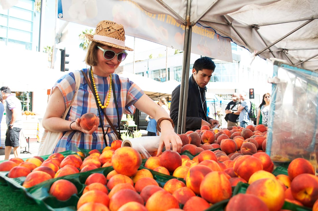 KEEN ON PEACHES: Coralie Winn, one of the GOOD Exchange fellows, picks out some peaches from one of the stands at the Downtown Farmers' Market on Wednesday morning. The fellows were at the market to learn about its storied history. (Paul Alvarez Jr. editor@www.smdp.com)