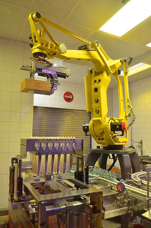 Manufacturing facilities that do not depend on human labor to get work done may have some energy saving benefits but are certainly not beneficial overall considering the impact widespread adoption would have on needed jobs. Pictured: a Robotic arm loading Coca Cola bottles into boxes and loading the boxes onto an assembly line. (Tom Maglieri, courtesy Flickr)