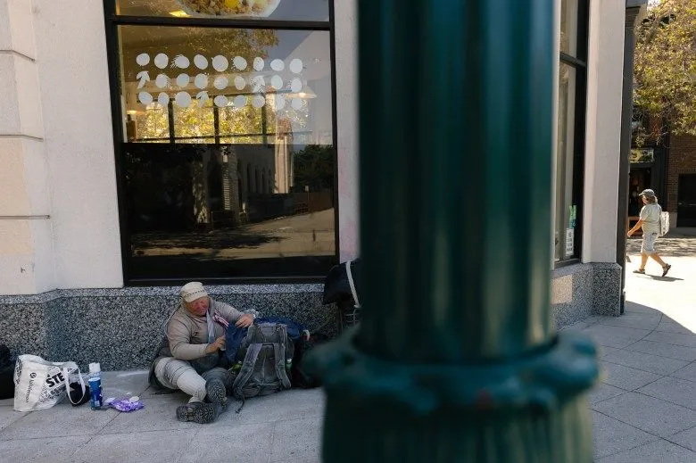 Roberta Titus, 67, wearing a beige hat, goes their belongings while sitting outside a juice shop on Front Street in Santa Cruz on Aug. 7, 2024. Photo by Manuel Orbegozo for CalMatters