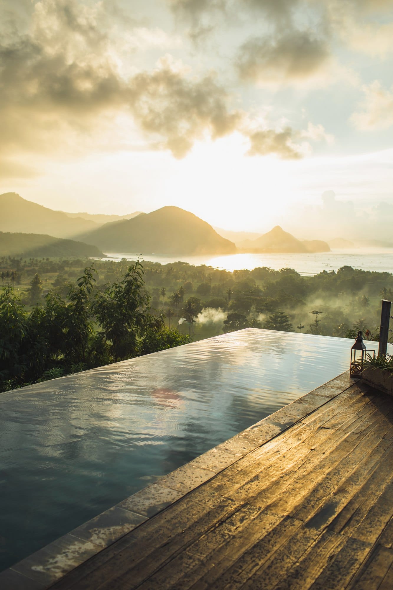 Infinity pool with amazing mountain and ocean view at sunset. Sun rays and mist. Cloud reflection