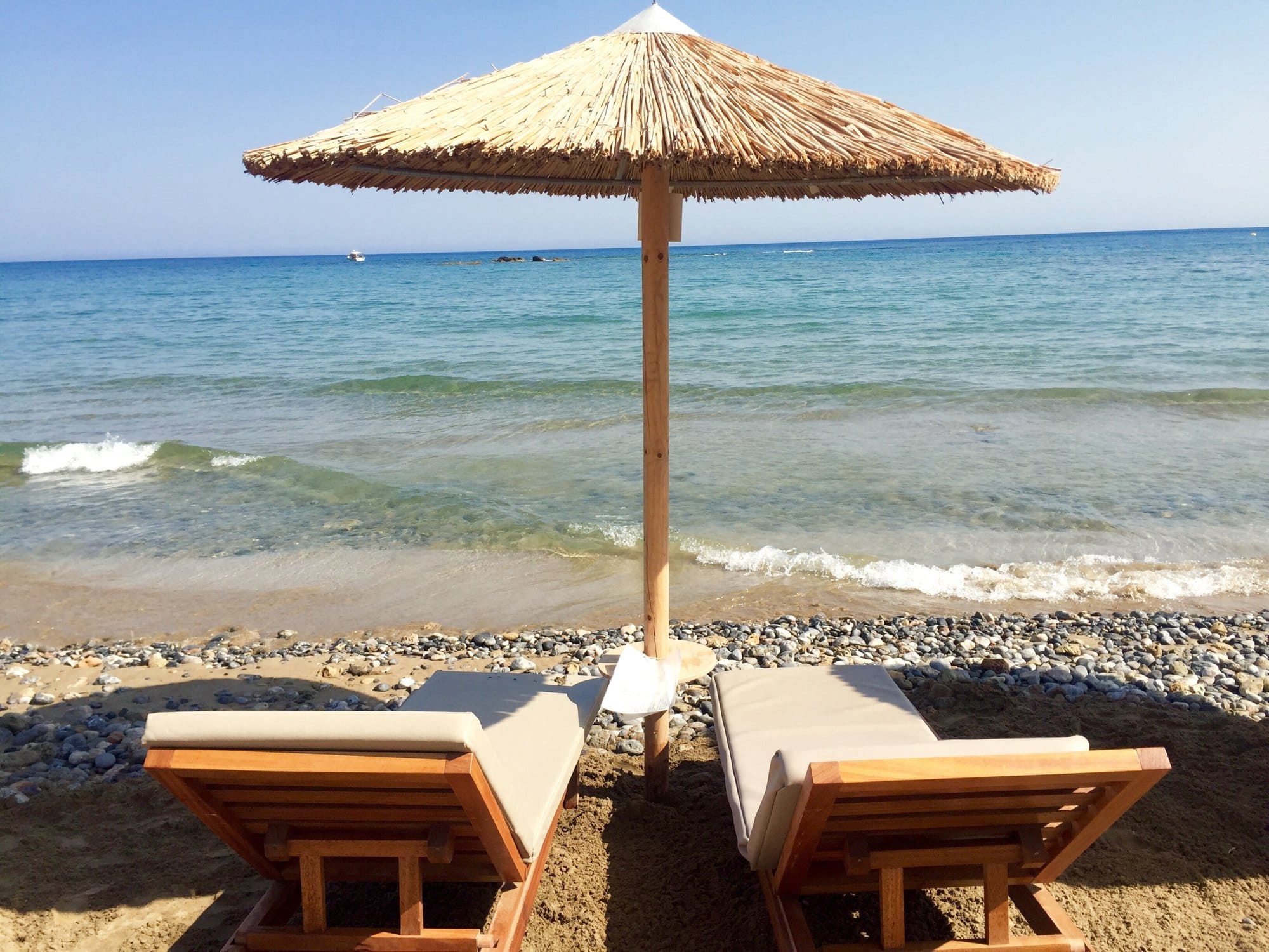 Two sunbeds and a thatched roof umbrella on the beach in Crete