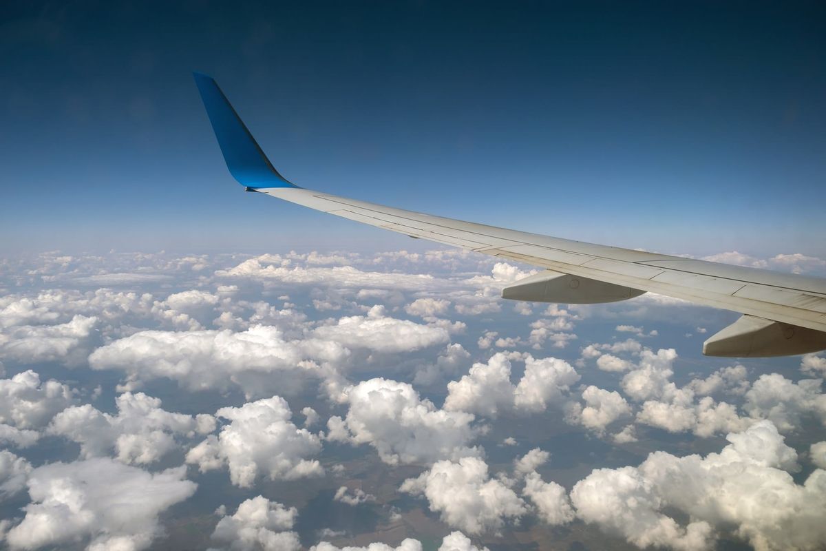 View of jet airplane wing from inside flying over white puffy clouds in blue sky