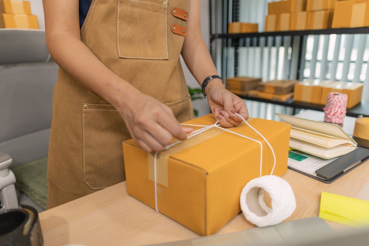 Close-up of young woman tying string around a cardboard box for shipping at her home office