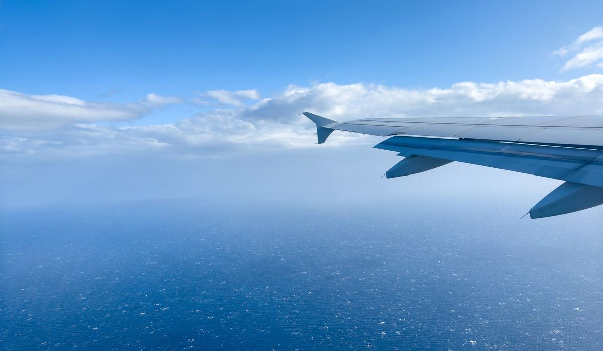 Plane flying over rippled sea, view from airplane window, fluffy cloudscape and blue sky