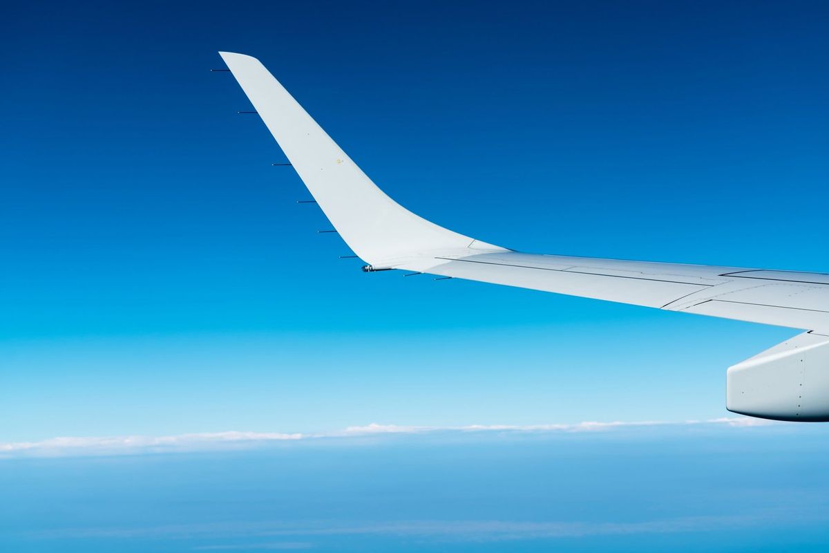 Wing of plane over white clouds. Airplane flying on blue sky. Scenic view from airplane window
