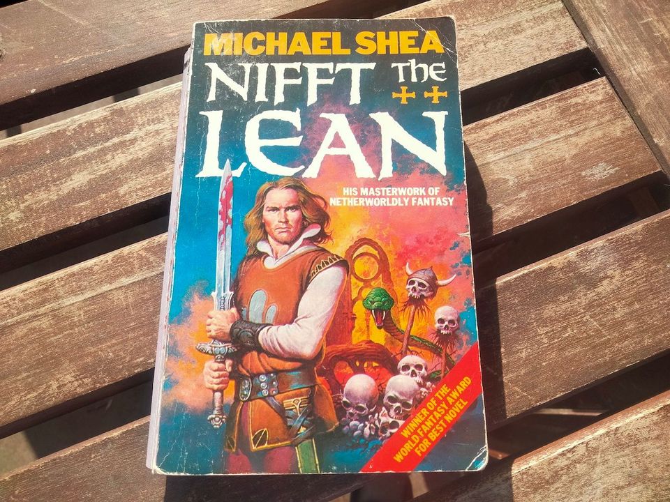 A man in medieval clothes clutches a bloody blade. Behind him is a pile of skulls and an emerald serpent.