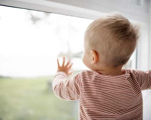 child in red and white striped shirt looking out the window