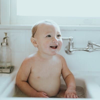 topless baby lying on white ceramic bathtub