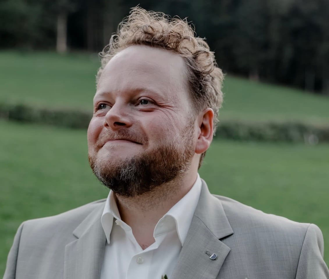 Franz-Alois Fischer steht vor einer grünen Wiese und dahinter angrenzendem Wald.