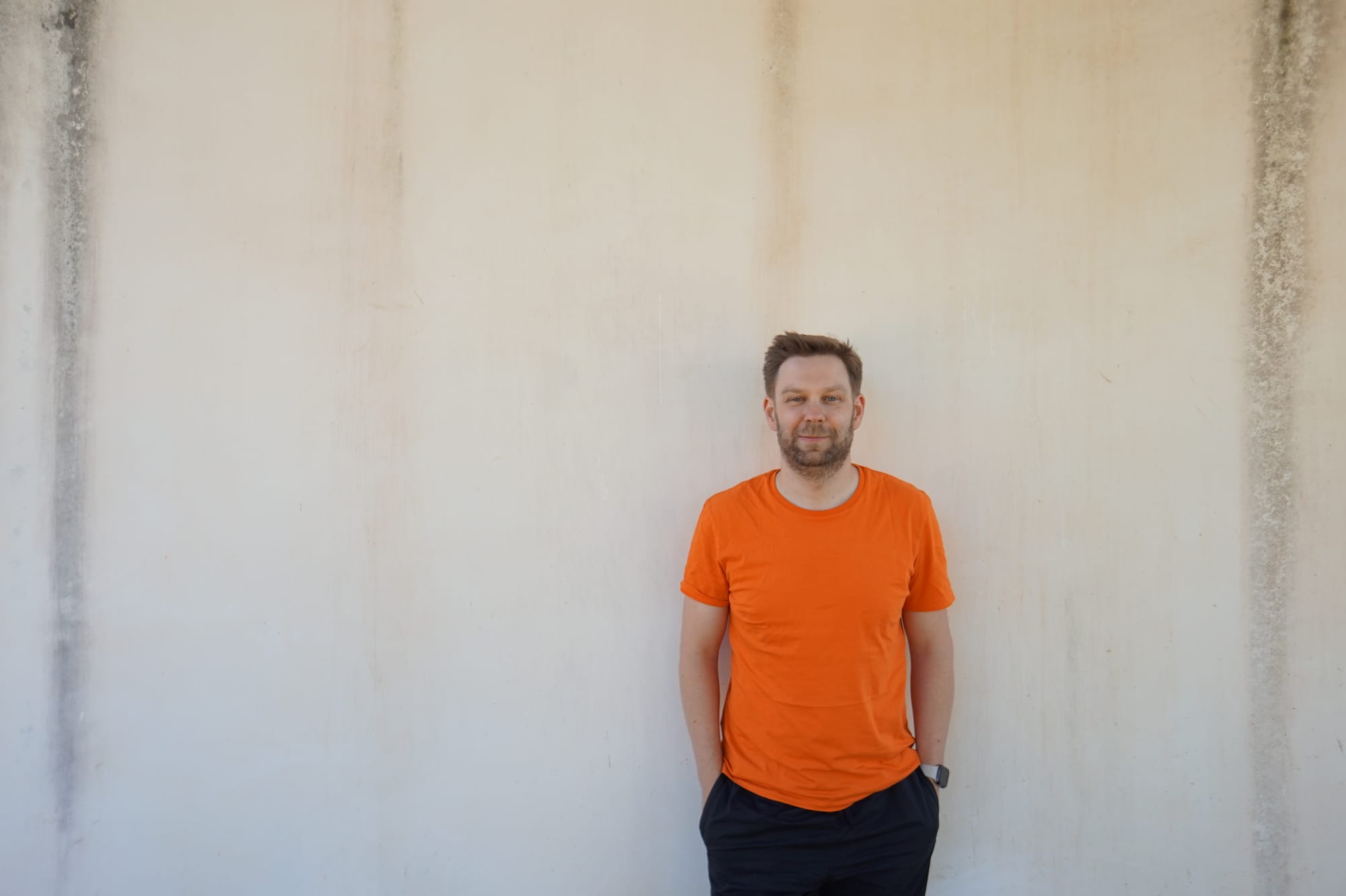Oliver Voigt steht in einem orangen T-Shirt vor einer Waschbeton-Wand.