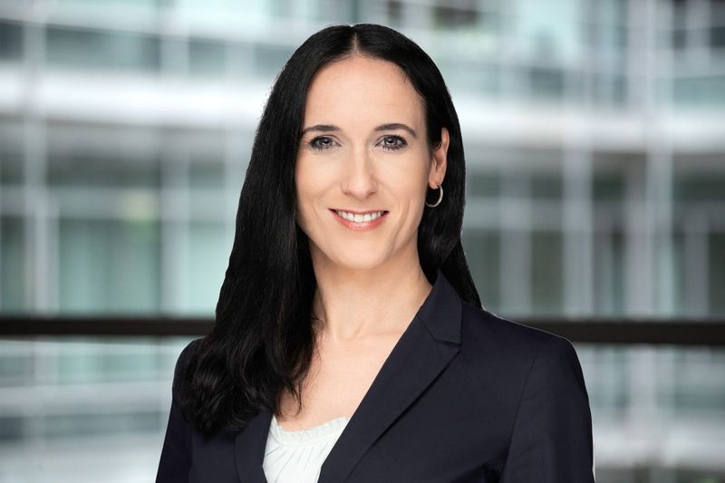 Melanie Kramp-Gerstner im Portrait-Format vor einem verschwommenen Glas-/Stahlhintergrund.