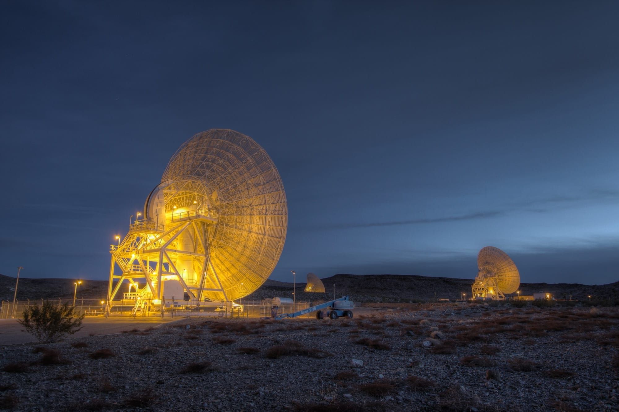 Antenă radio uriașă luminată noaptea la complexul Goldstone Deep Space Communications