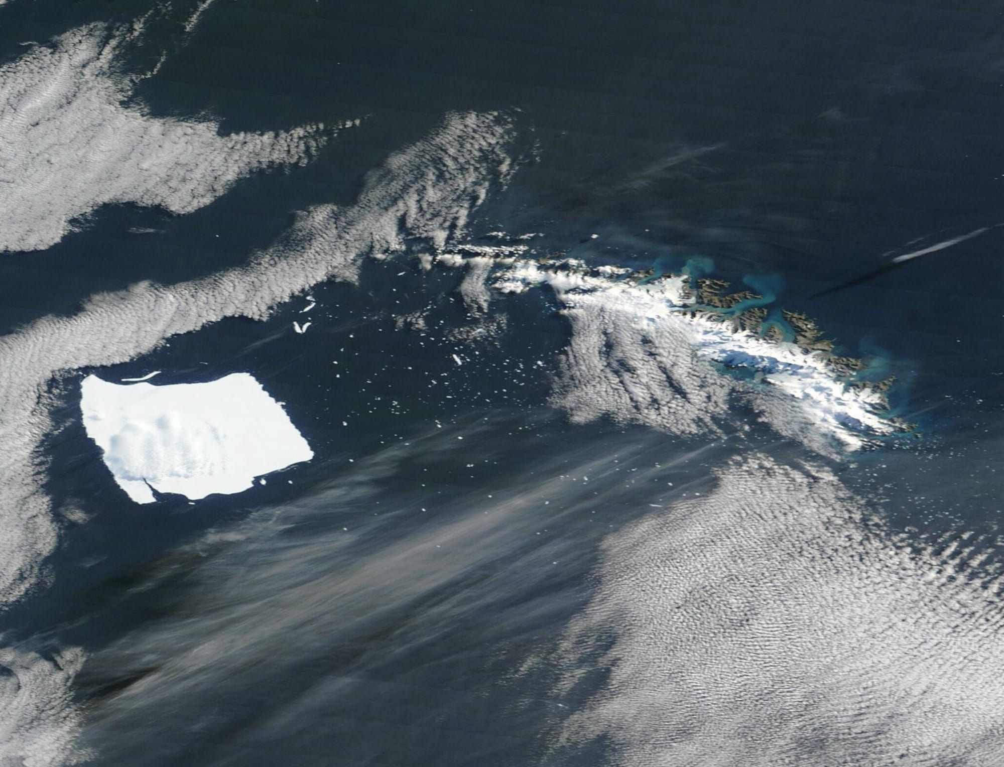 Imagine din satelit cu aisberguri albe plutind și ancorate în apele înconjurate de gheață ale Antarcticii