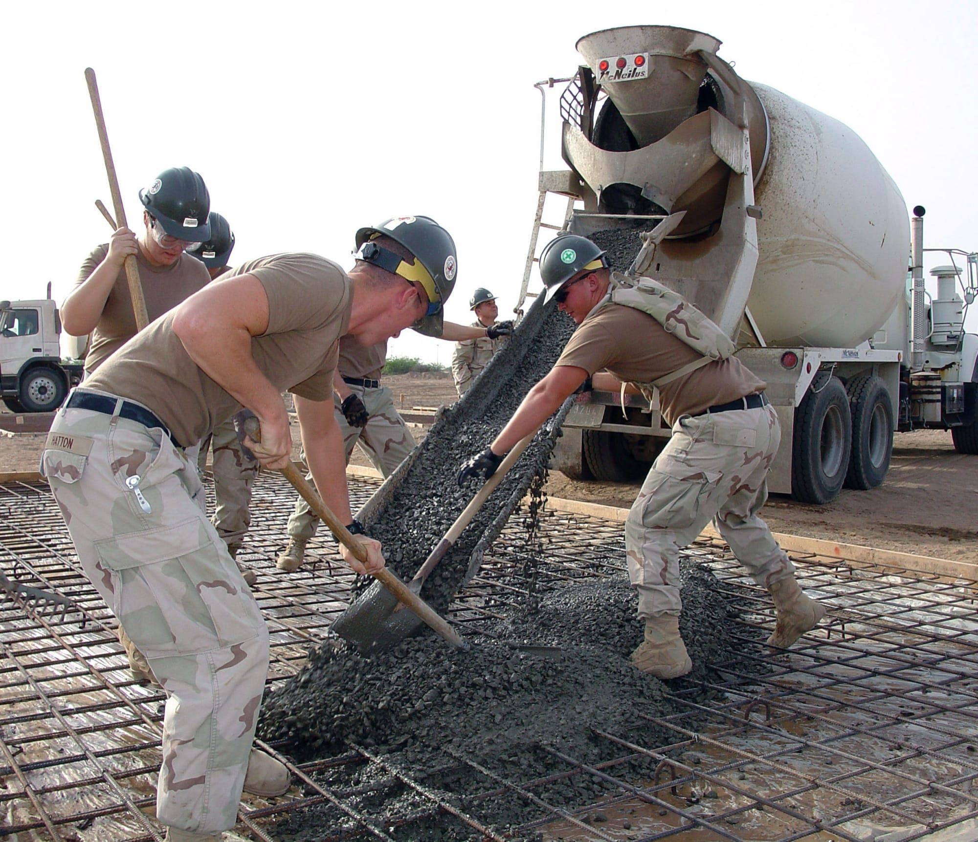 Muncitori turnând beton proaspăt pe o structură de armătură metalică, pe un șantier de construcții
