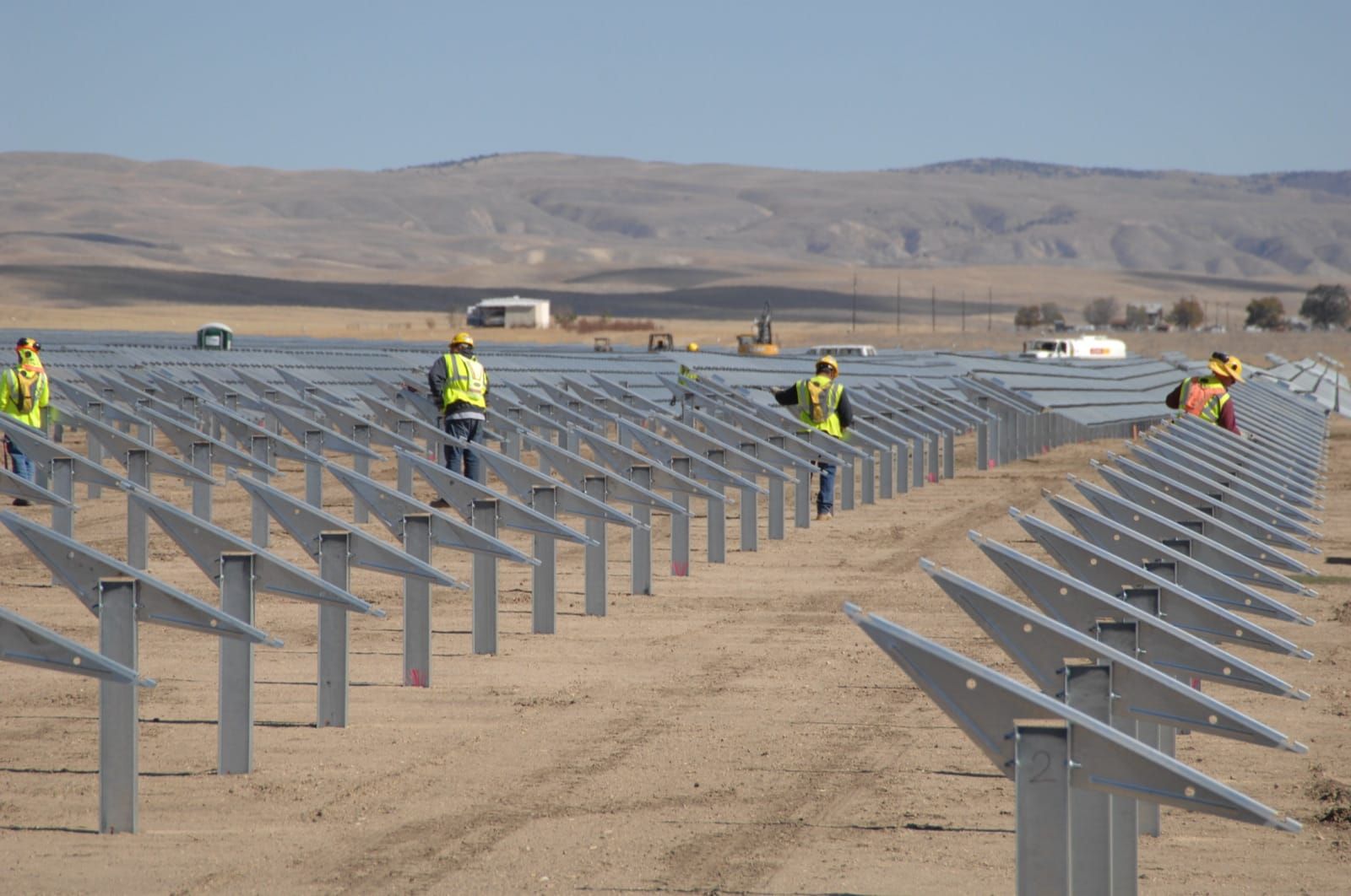 Muncitori instalează rânduri de panouri solare într-un parc fotovoltaic la scară mare