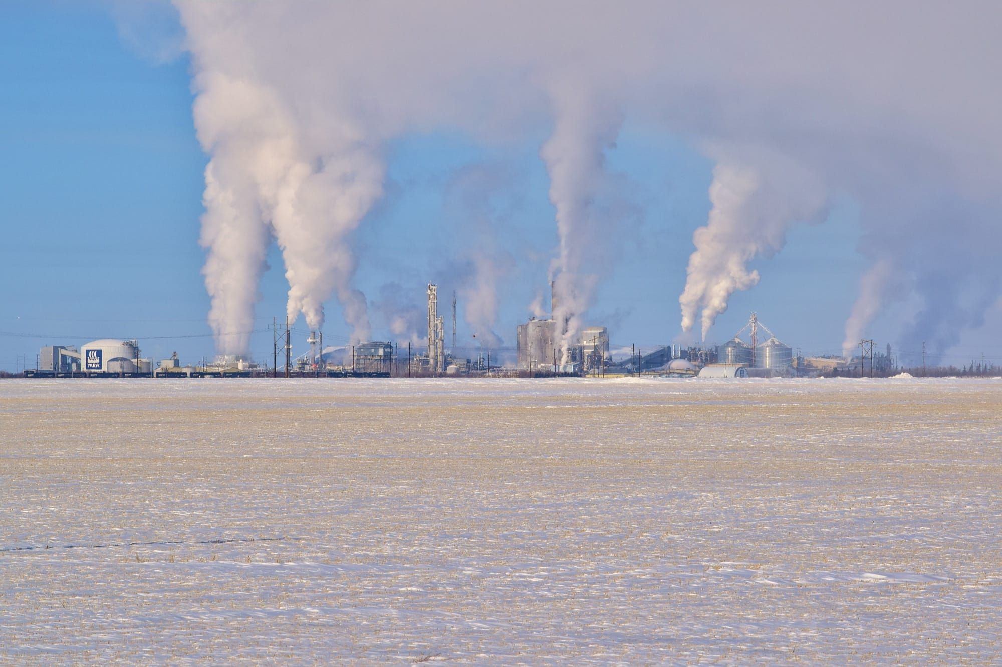 Fabrică industrială Yara cu coșuri care emit aburi pe fondul unui cer senin de iarnă