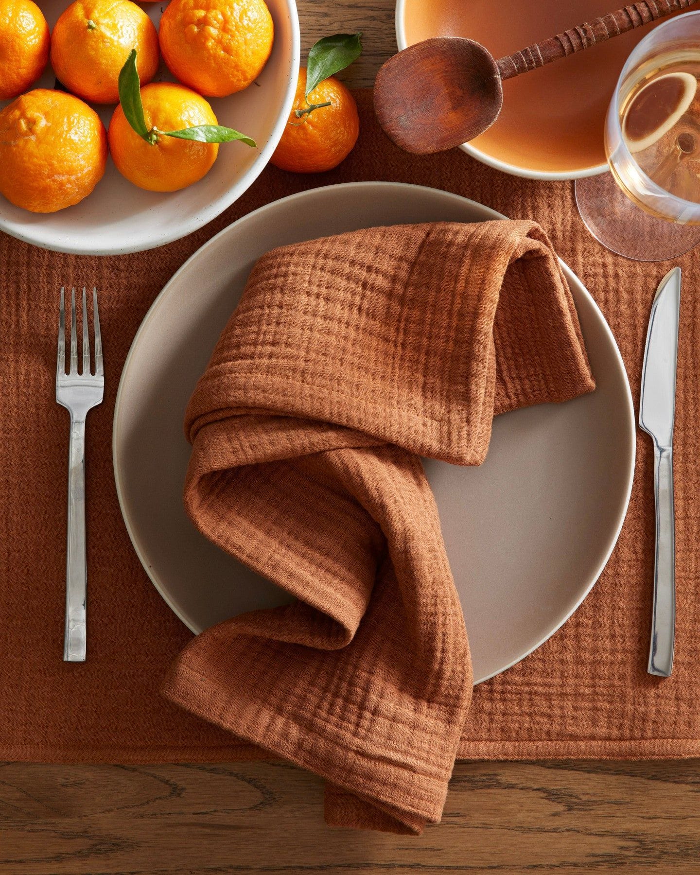 A tablescape with orange linens, a bowl of oranges, and some silverware