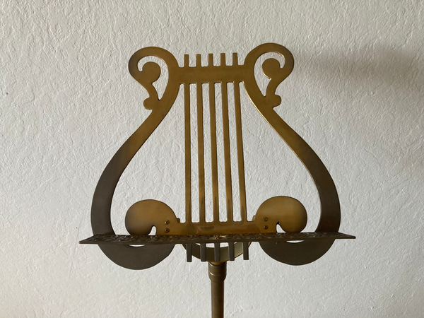 An antique brass music stand in the shape of a lyre in front of a grey wall