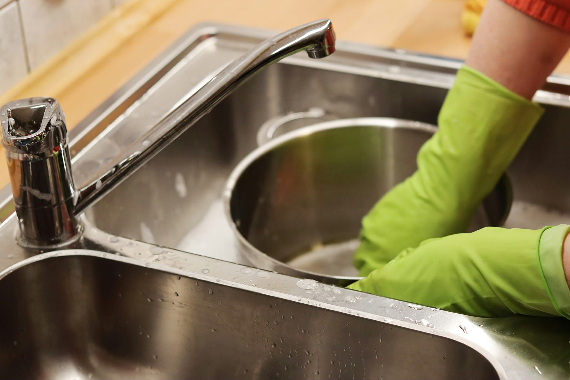 A person washing a pot in a sink. They are wearing green rubber gloves. 