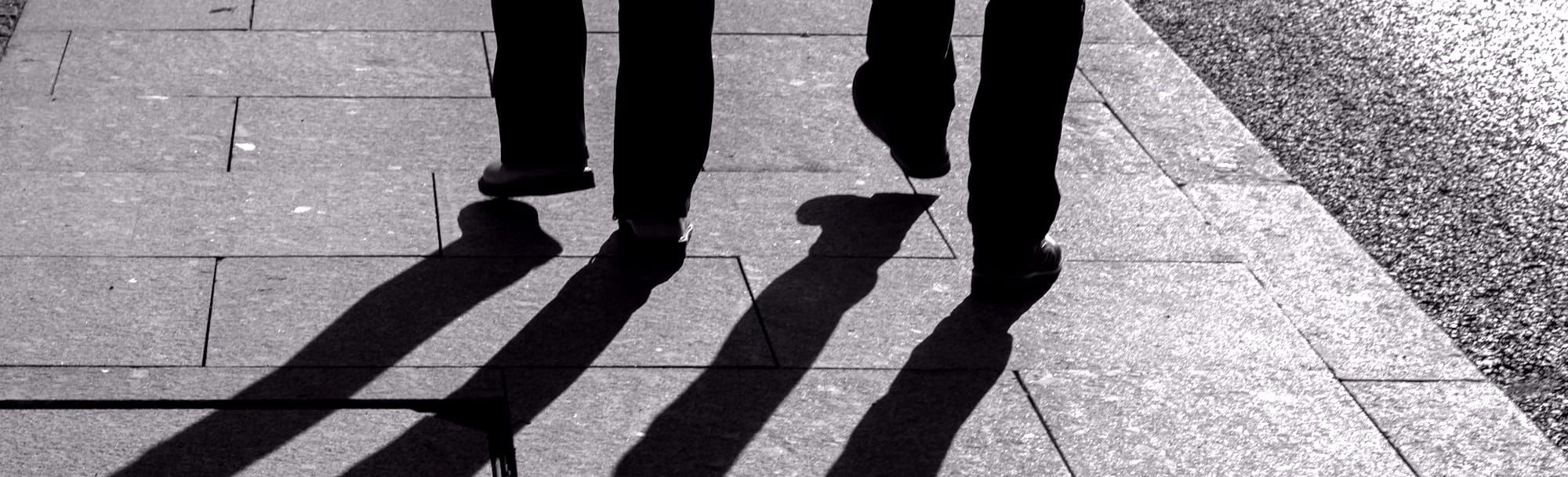 Two silhouetted men walking, their shadows stretching away from them.