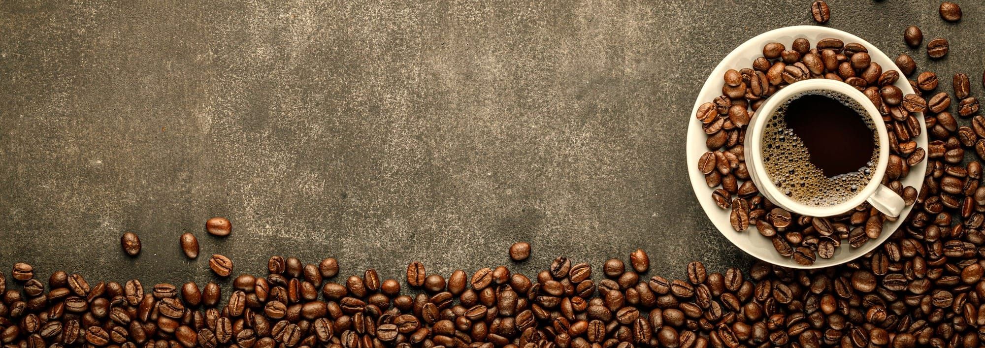 Coffee in cup on saucer sitting on concrete surface surrounded by coffee beans.