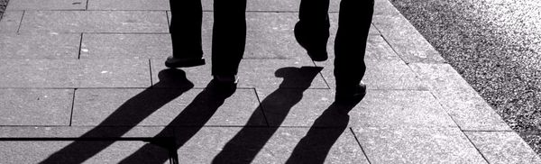 Two silhouetted men walking, their shadows stretching away from them.