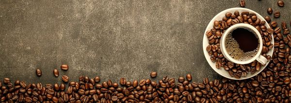 Coffee in cup on saucer sitting on concrete surface surrounded by coffee beans.