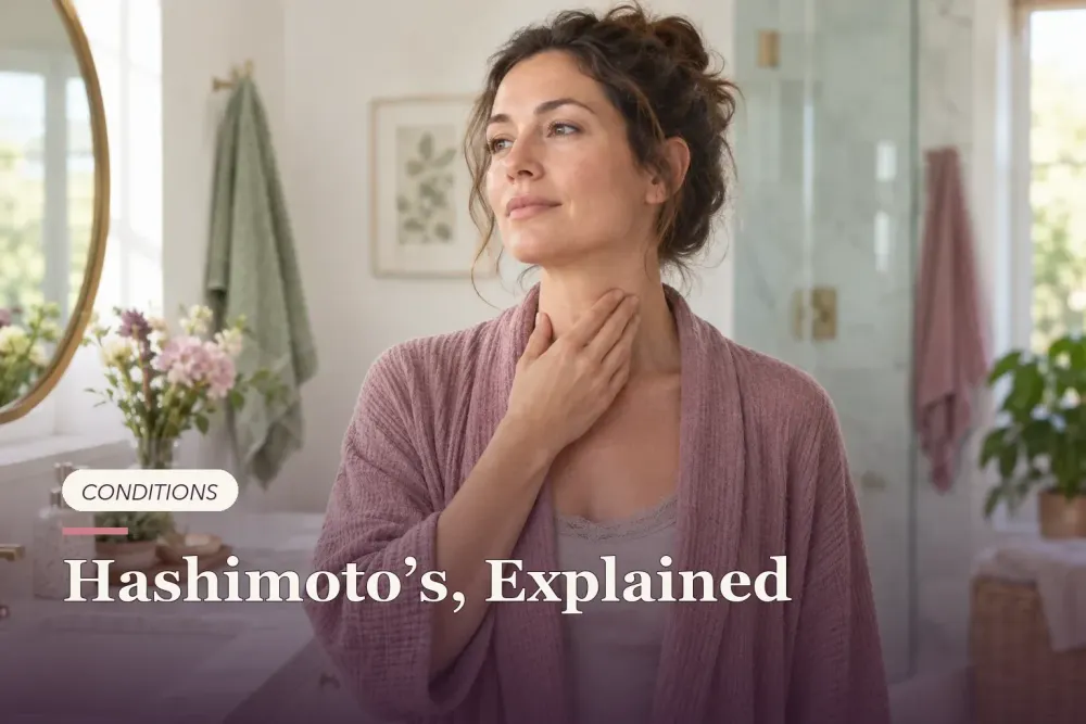 A woman gently touching the front of her neck in a bright bathroom.