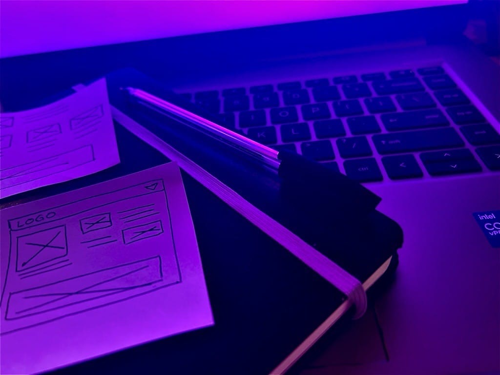 Hand drawn wireframes and a notepad sitting on a laptop under blue light