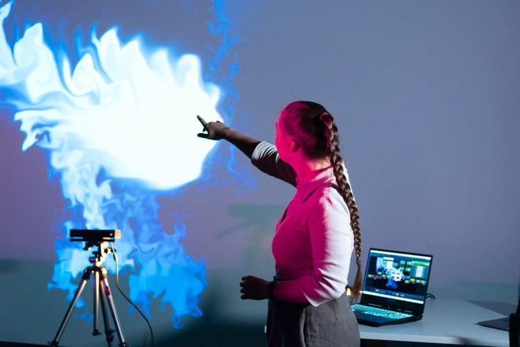 A person with long braided hair controls a projection of a smoke-like visual using her hand, via a sensor and computer