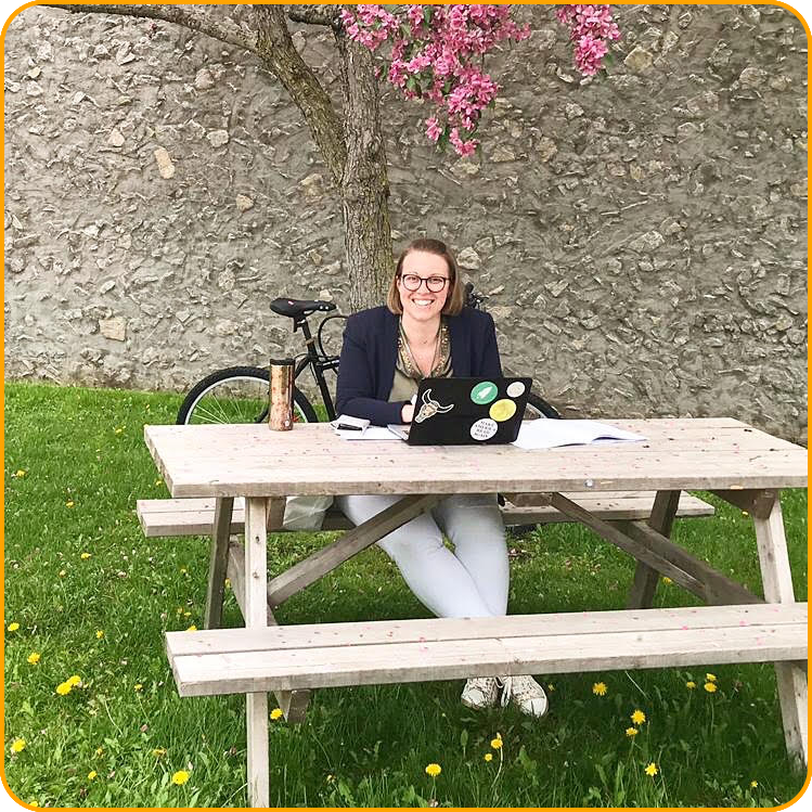 Eva-Maria, a student from Austria, takes a break outside, sitting at a picnic table under a pink flowering tree.