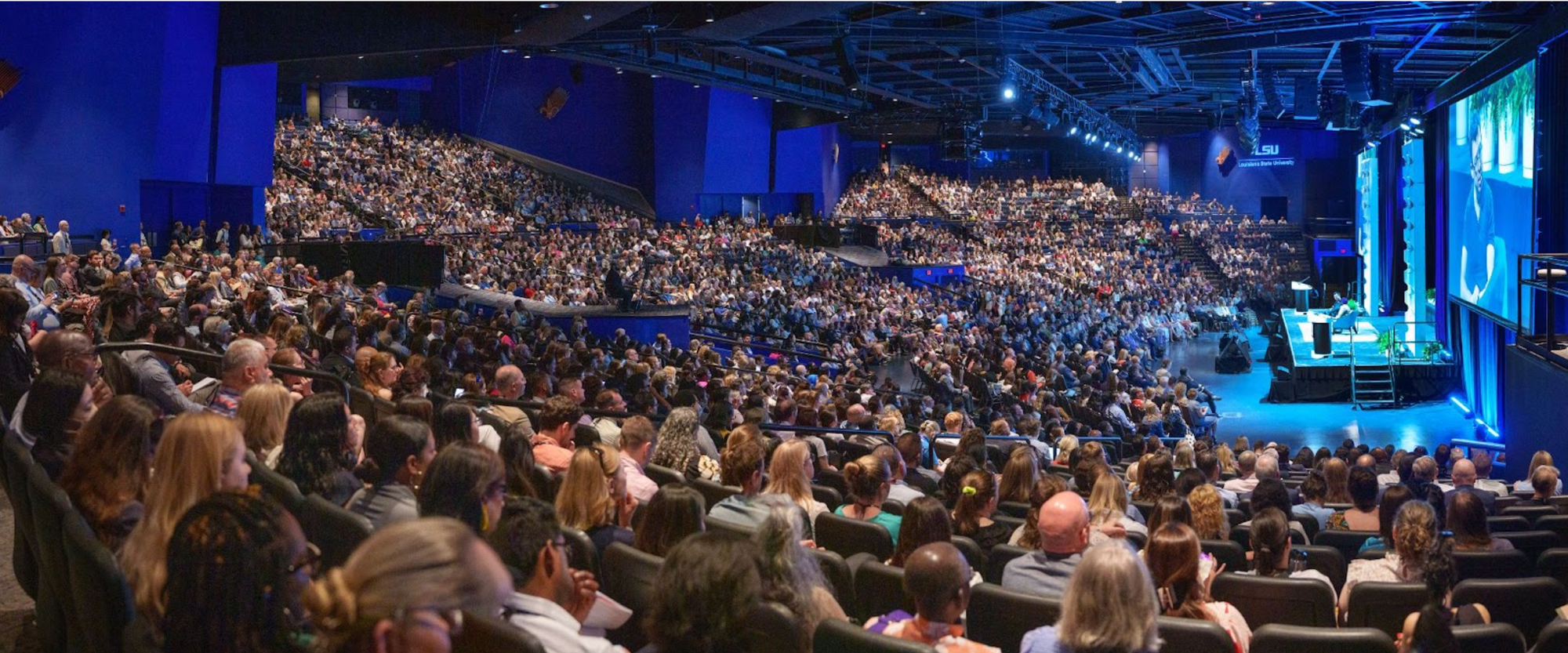 A large crowd in stadium seating watching Luis von Ahn speak on stage