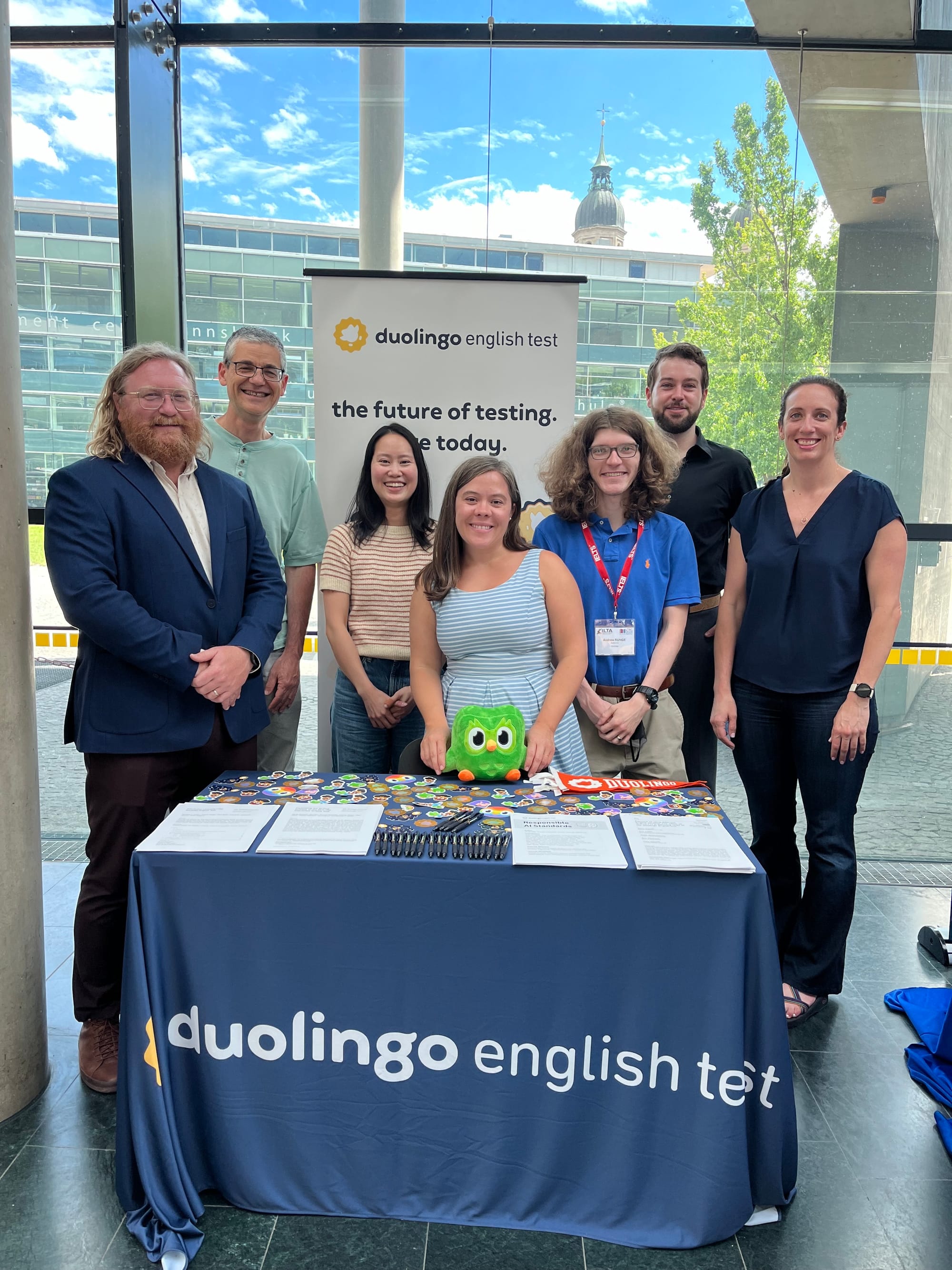 DET researchers standing around the DET’s exhibit booth, covered with a blue table cloth