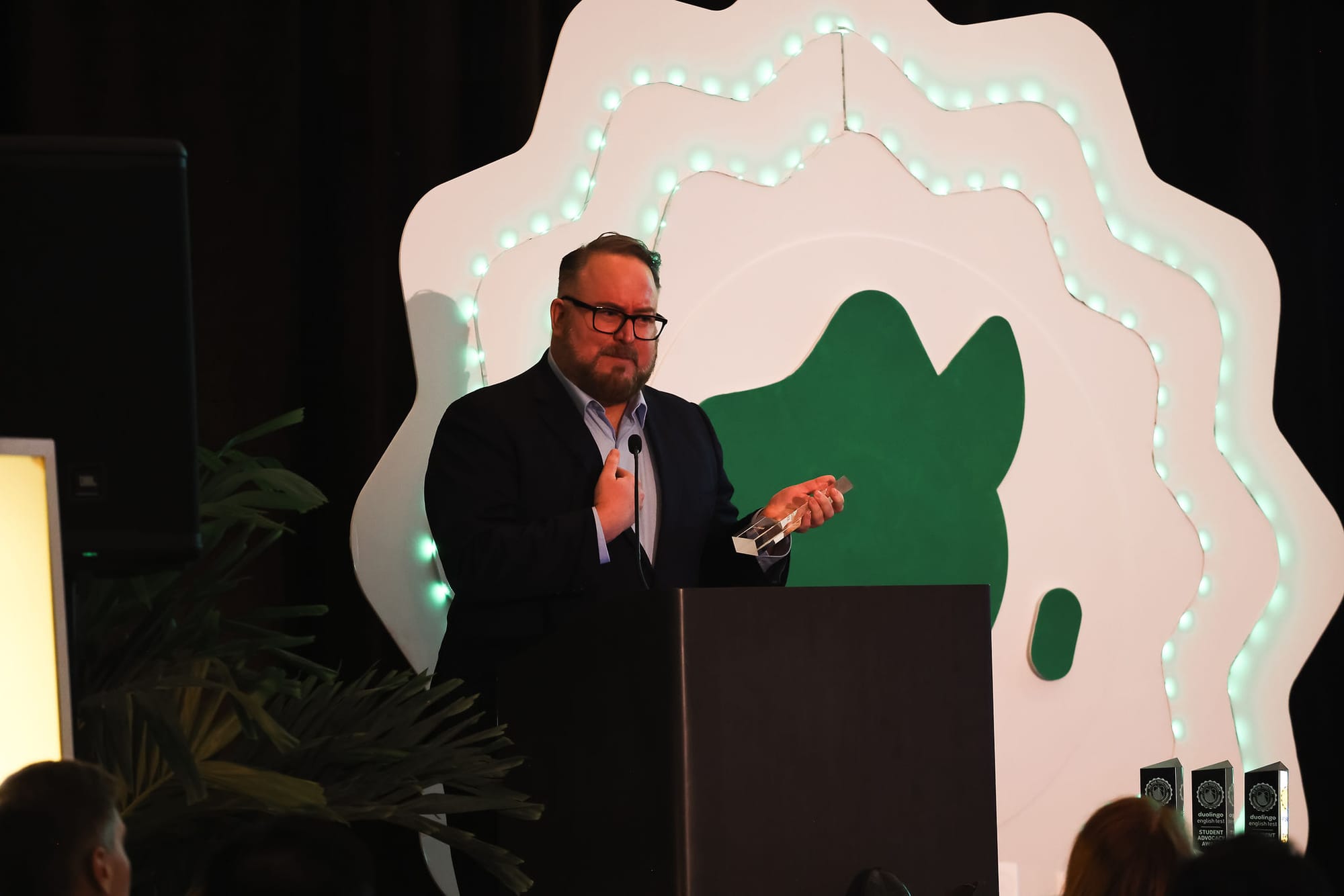 A man stands behind a podium on stage, holding a We Rise Together award