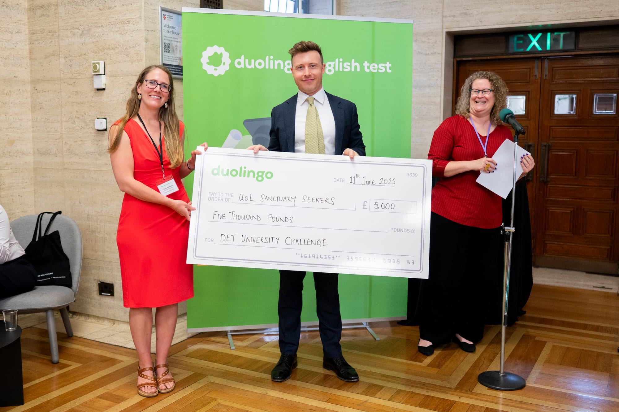 Fiona stands on the left, holding a large cheque. A man is also holding the check, and a woman is standing to the right, smiling.