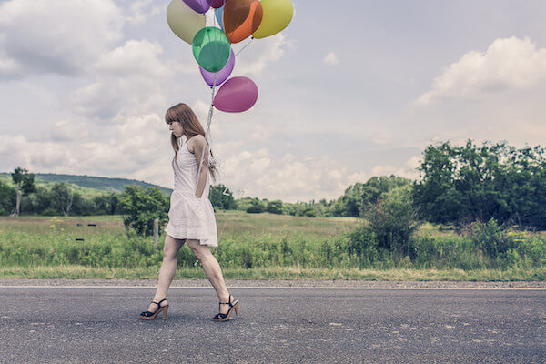 A woman walking along a road carrying a lot of colorful balloons