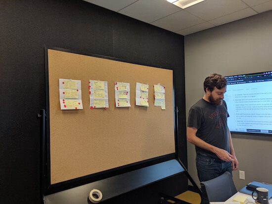 A man stands in front of a bulletin board covered with papers and Post-It notes.