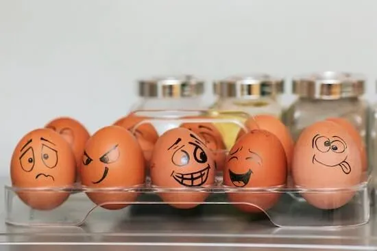A photograph of a tray full of eggs. Each egg has a different face drawn onto it.