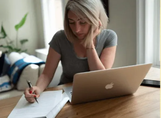 Rachel sits at a table with her laptop and printed out report, which she's reading and making notes on.