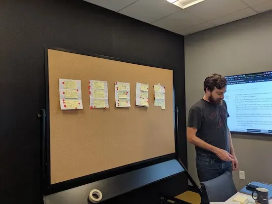 A man stands in front of a bulletin board covered with papers and Post-It notes.