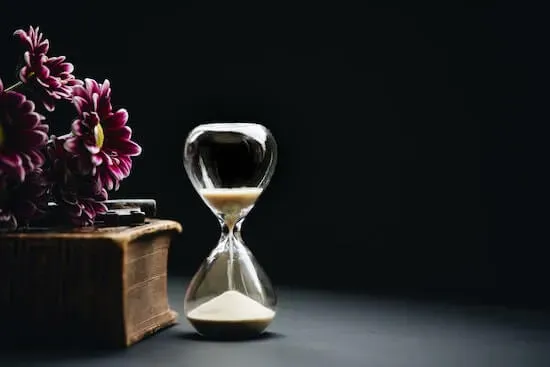 An hourglass with sand running out next to flowers on a table.