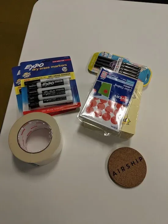 A table with masking tape, whiteboard markers, dot stickers, and Post-It notes.