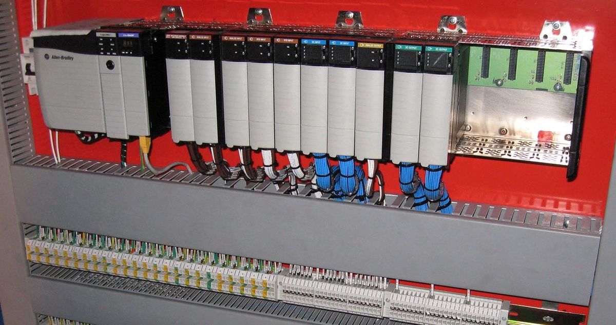 An Allen-Bradley MicroLogix 1100 programmable controller and 1762-series expansion modules mounted in a red control cabinet.