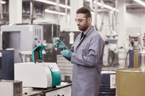 A laboratory technician in a coat and safety glasses prepares a liquid sample for a benchtop near-infrared (NIR) analyser.
