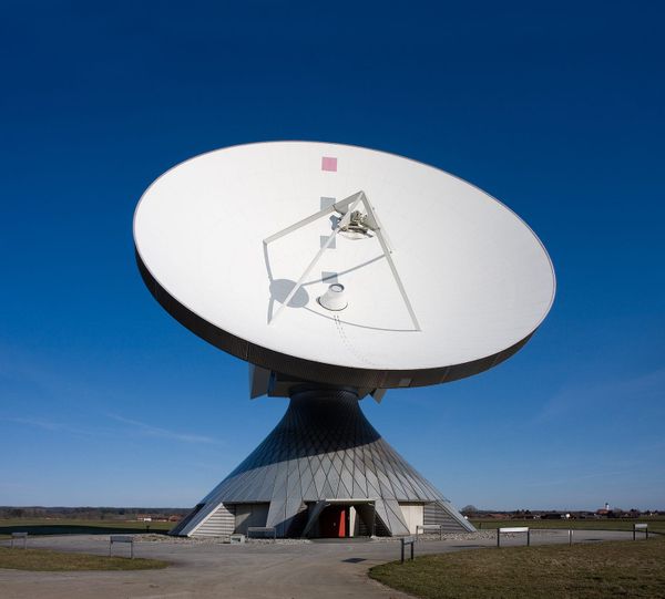 A large white satellite dish antenna at the Raisting Earth Station in Germany, set against a clear blue sky.