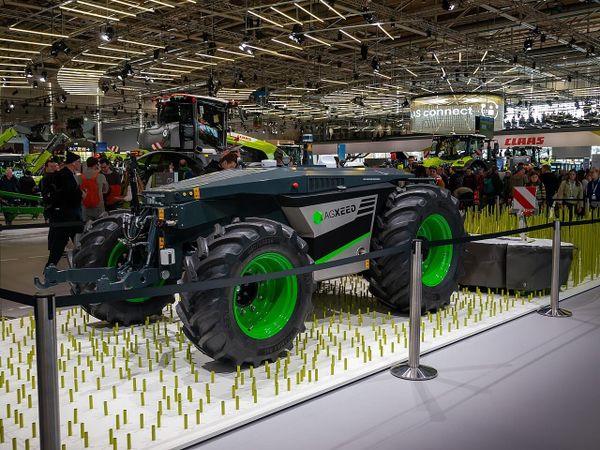 AgXeed autonomous tractor with bright green wheel rims exhibited on a pegged display platform at an indoor agricultural trade show.