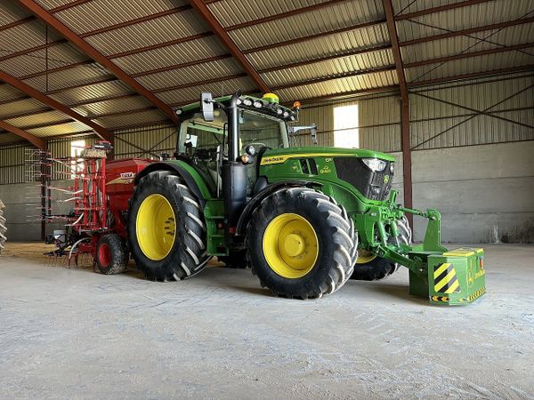 A green John Deere tractor with mechanical weeding implements parked inside a large agricultural shed.