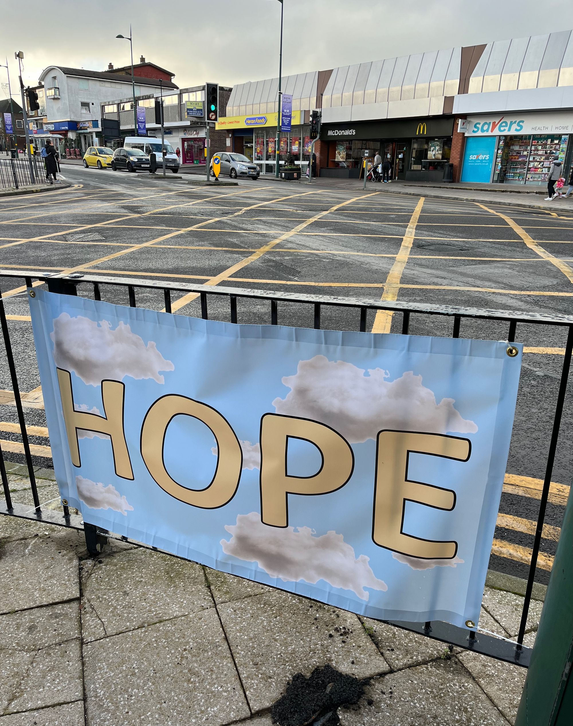 Poster with the word HOPE against a blue sky background tagged to a railing in Northfield High St